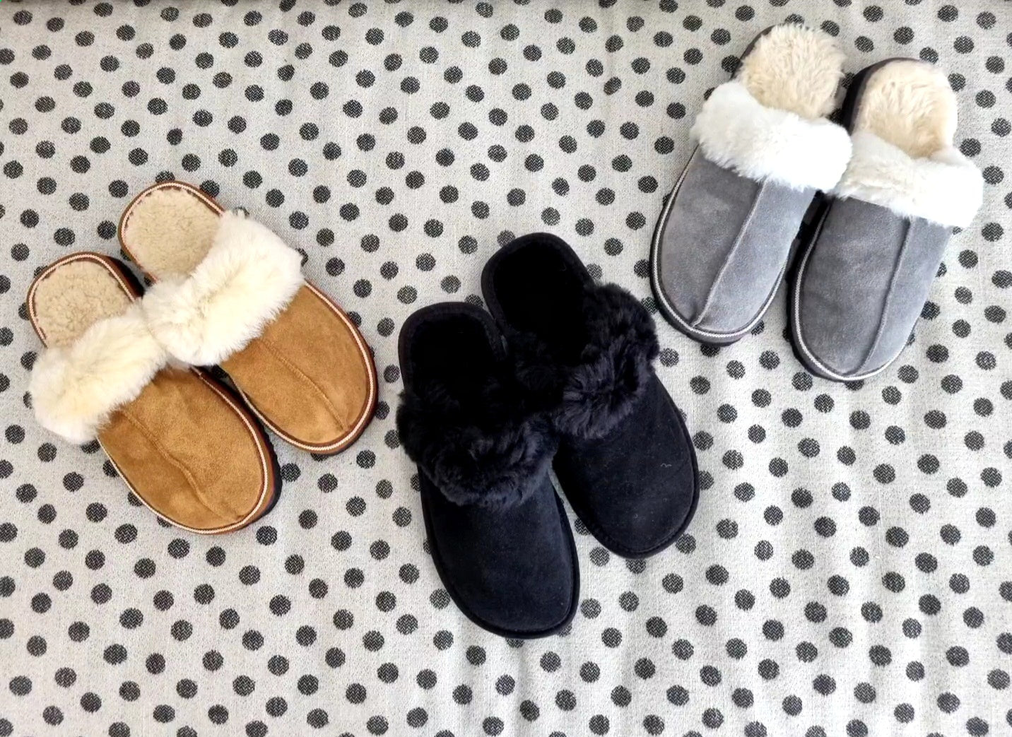 Tre par fårskinnstofflor med öppen häl från Jakobs Handmade i brunt, svart och grått med ullkant, placerade på vit filt med svarta prickar.