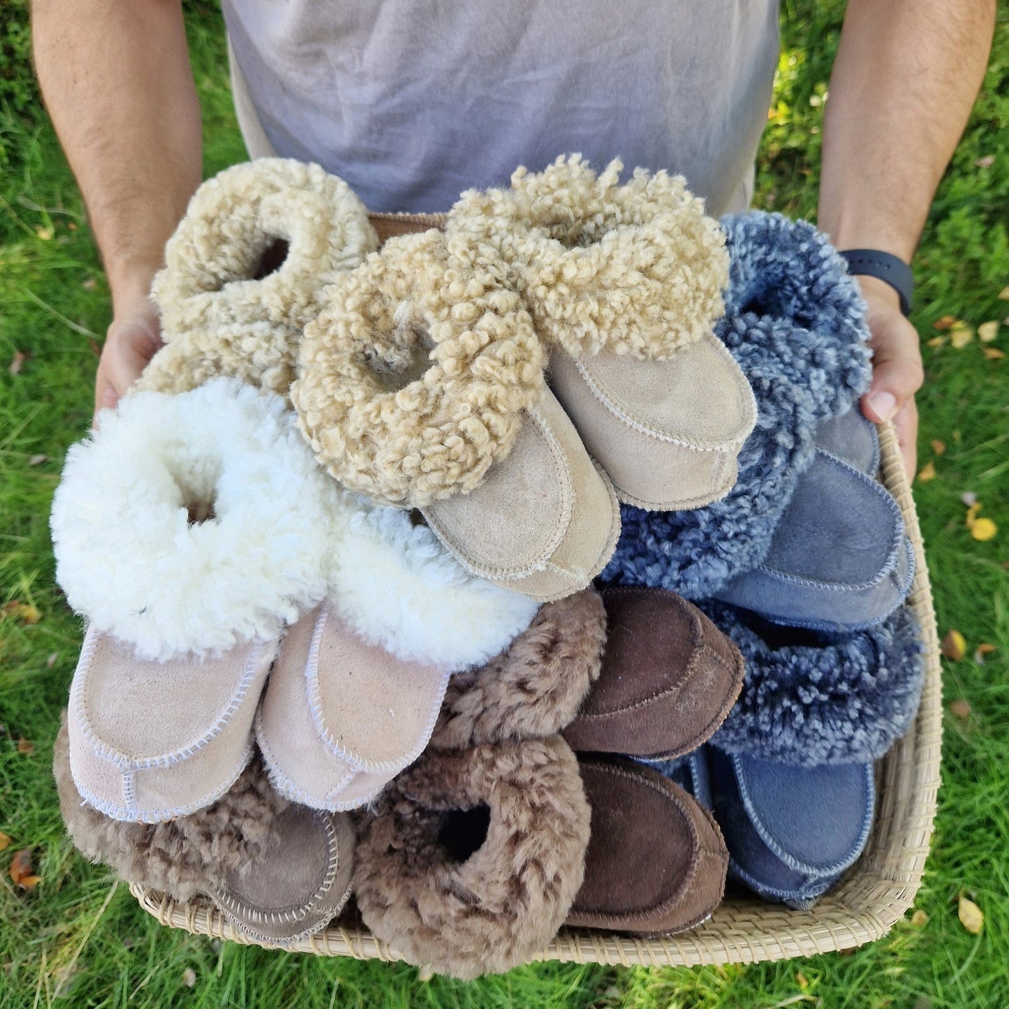 En korg fylld med handgjorda fårskinnstofflor från Jakobs Handmade i olika färger och storlekar för både barn och vuxna. Tillverkade i äkta svenskt fårskinn med mjuk och värmande krage.