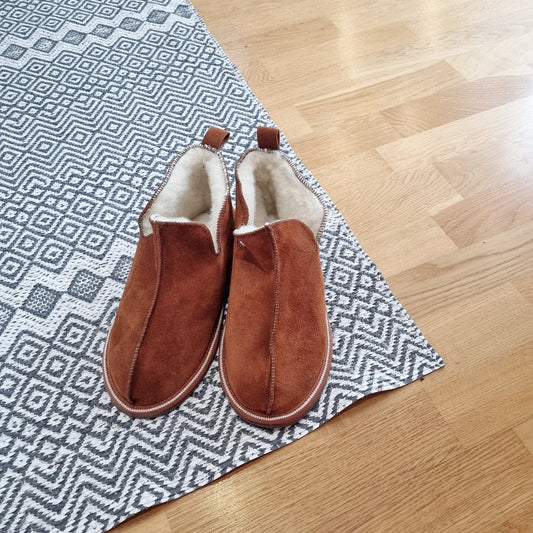 Kosmos merinoullstofflor i kanelbrun färg från Jakobs Handmade, placerade på mönstrad matta i hemmiljö, tillverkade i mjuk mocka med varm fårskinnsfodring.