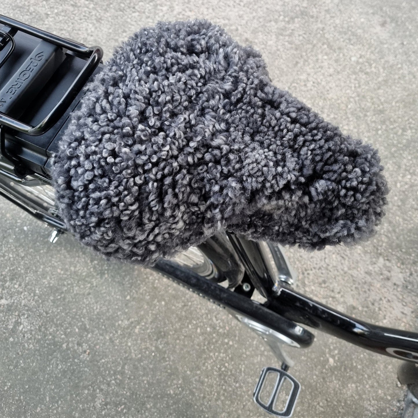 Mörkgrått fårskinnsadelskydd på svart el cykel för extra komfort och värme vid cykling.