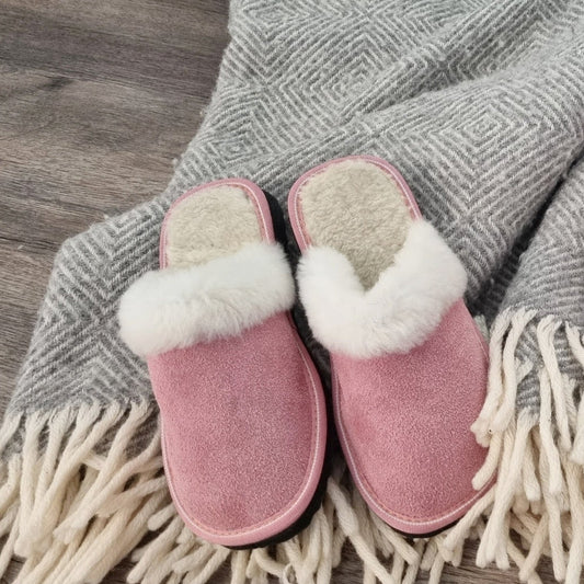 Två par rosa ullstofflor från Jakobs Handmade – Elpida slip-in tofflor med vit fårskinnskant och Kosmos ankelhöga tofflor, placerade på en grå filt med fransar för en varm och hemtrevlig känsla.