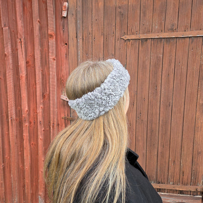 Kvinna med långt blont hår bär ett grått pannband i äkta fårskinn från Jakob’s Handmade framför en trävägg.