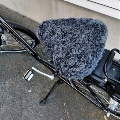Grått fårskinnsadelskydd i äkta lammskinn på en svart cykel, ger extra komfort och värme vid cykling.