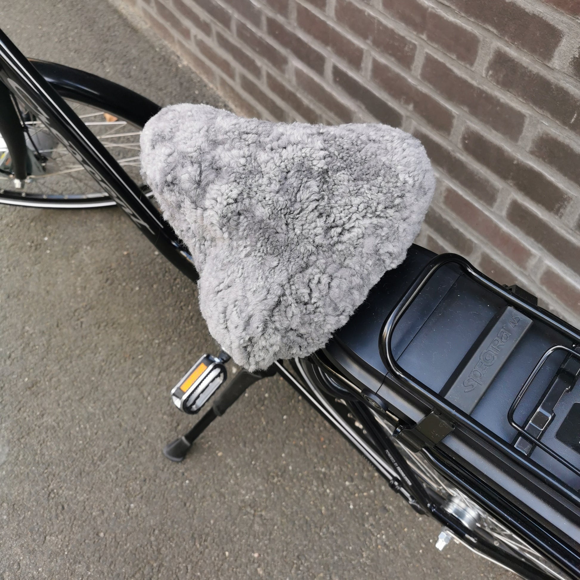 Ljusgrått fårskinnsadelskydd i äkta lammskinn på svart cykel, ger mjukare och varmare cykelturer.