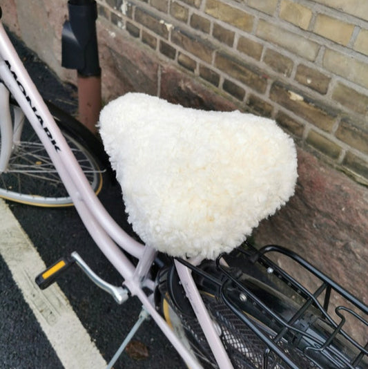 Vitt fårskinnsadelskydd monterat på en cykel som står parkerad vid en tegelvägg.