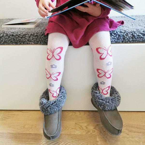 Barn sitter och läser bok iförd handgjorda grå fårskinnstofflor från Jakobs Handmade. Tofflorna är tillverkade i äkta svenskt fårskinn med mjuk och värmande krage.