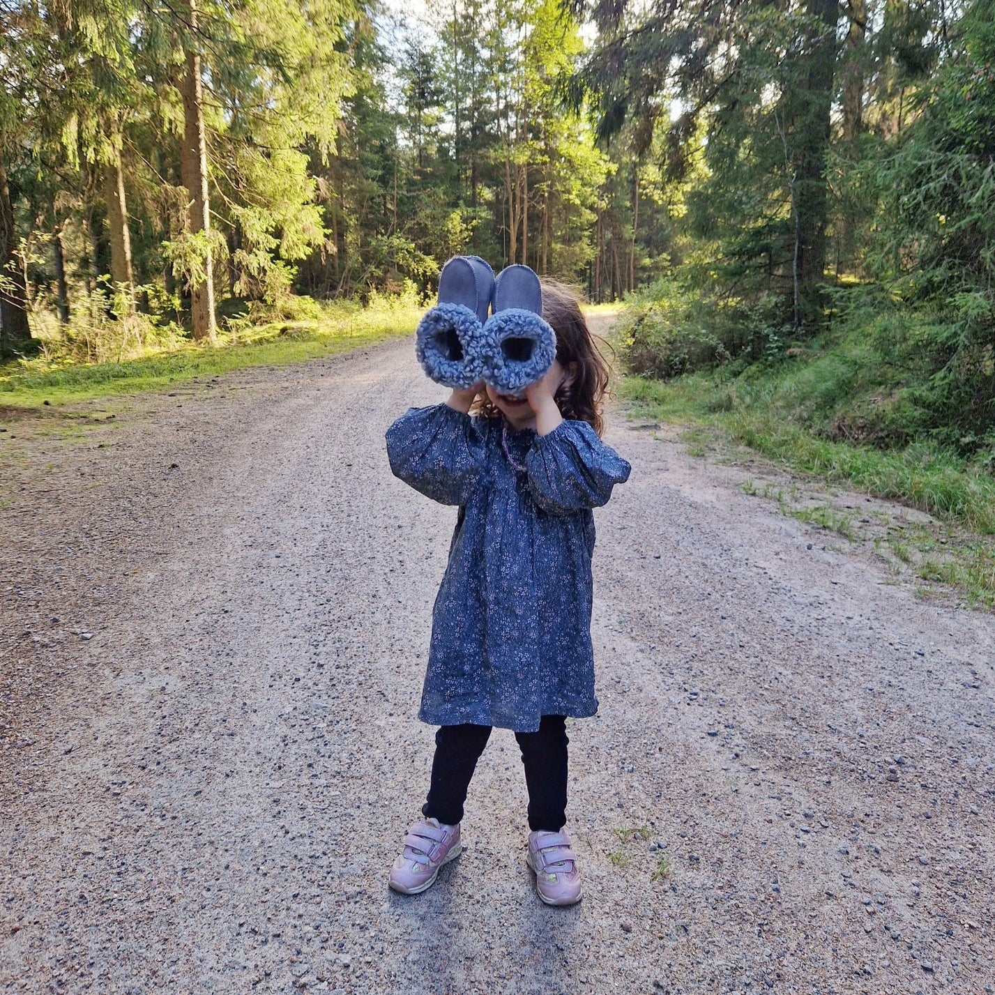 Barn håller upp ett par handgjorda grå fårskinnstofflor från Jakobs Handmade, tillverkade i äkta svenskt fårskinn med mjuk värmande krage.