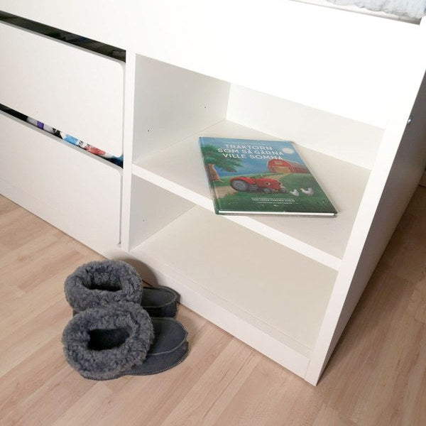 Handgjorda grå fårskinnstofflor för barn från Jakobs Handmade, placerade vid en vit barnsäng. Tofflorna är tillverkade i äkta svenskt fårskinn med mjuk värmande krage.
