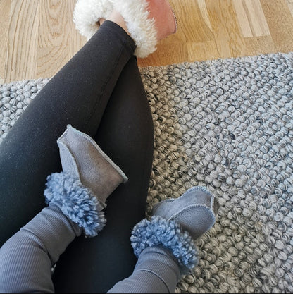 Vuxen och barn bär handgjorda fårskinnstofflor från Jakobs Handmade, i rosa och grått. Tofflorna är tillverkade i äkta svenskt fårskinn med mjuk värmande krage för komfort och värme.