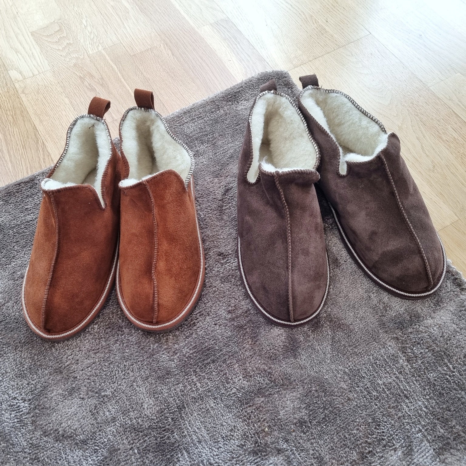 Kosmos merinoullstofflor i färgerna kanel och brun från Jakobs Handmade, handgjorda fårskinnstofflor med värmande ull, placerade på en matta.