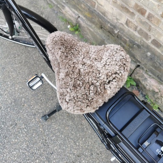 Ljusbrunt fårskinnsadelskydd på svart cykel för bekvämare och varmare cykelturer.