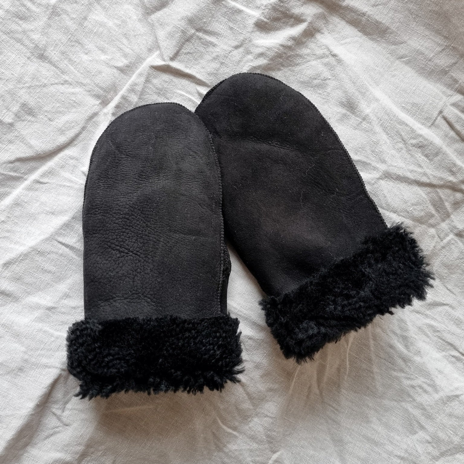 Svarta fårskinnsvantar med svart ullfoder och uppvikbar mudd, unisexmodell för dam och herr, värmande och slitstarka för vinterbruk.