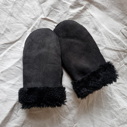 Svarta fårskinnsvantar med svart ullfoder och uppvikbar mudd, unisexmodell för dam och herr, värmande och slitstarka för vinterbruk.